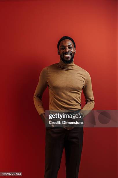 confident young businessman smiling with hands in pockets on red background - hands in pockets stock pictures, royalty-free photos & images