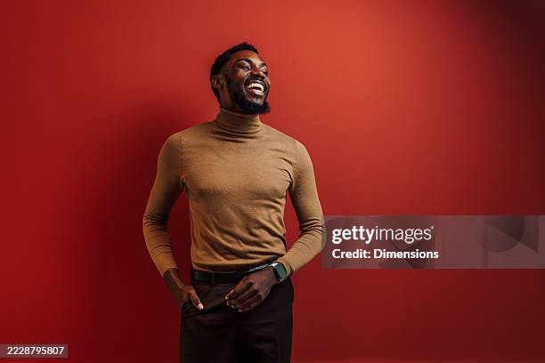 young businessman laughing looking away with hands in pockets on red background - turtleneck stock pictures, royalty-free photos & images