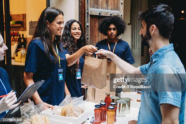 voluntarios que dan comida a personas necesitadas al aire libre - limosna fotografías e imágenes de stock