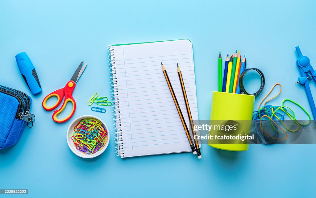 Multicolored stationary, school or office supplies banner shot from above, flat lay. Note pad, colored pencils, scissors and drawing compass, working or back to school concept on blue background