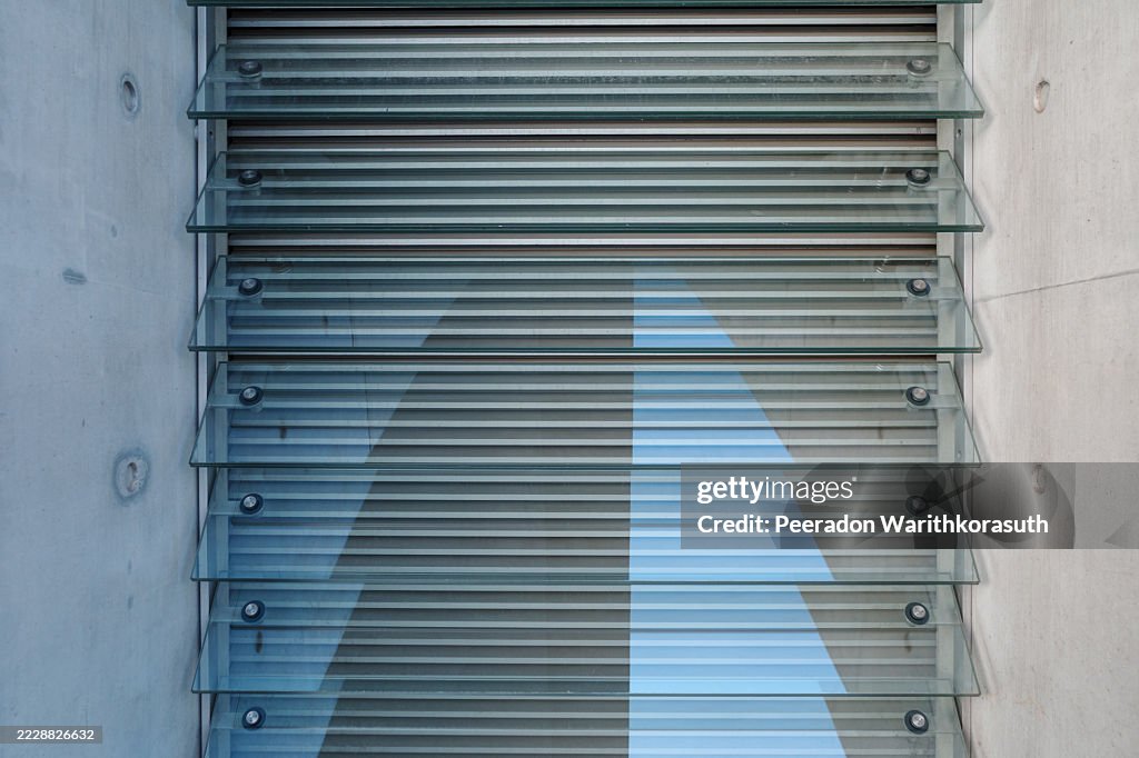 Horizontal glass louvers are mounted on a raw concrete wall, creating a strong linear pattern.