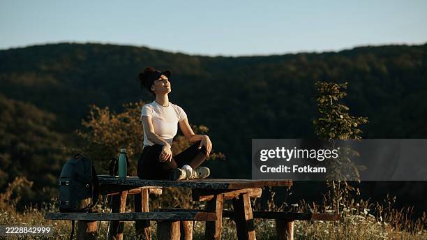 photo of a young and beautiful female mountaineer. he sits on a wooden bench and stretches his body before hiking. - semana imagens e fotografias de stock
