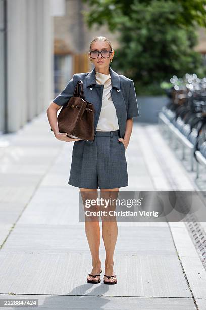 Justyna Czerniak wears brown suede Demellier bag, grey shorts, jacket, creme white top, sunglasses outside Herskind during Copenhagen Fashion Week...