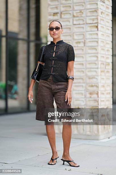 Guest wears a black, short-sleeved, sheer knit top with a high collar and decorative frog closures down the front. The top is paired with...