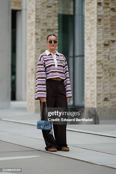 Guest wears hair styled in a sleek, pulled-back manner. Oval sunglasses with dark lenses and thin frames are worn. A striped, long-sleeve crop top in...