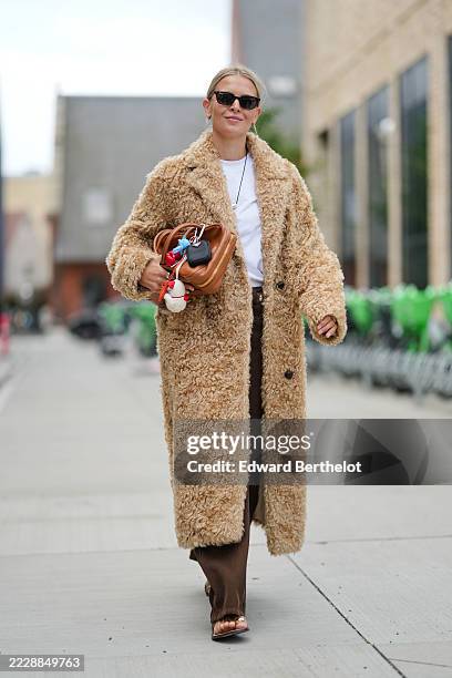 Guest wears a long, textured sheep fluffy fur, camel-colored faux fur coat with large buttons. Underneath, a white t-shirt is visible. Dark brown...