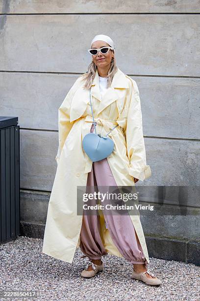 Guest wears yellow coat, rose pants, head scarf, sunglasses, blue Alaia bag outside Munthe during Copenhagen Fashion Week day three on August 06,...