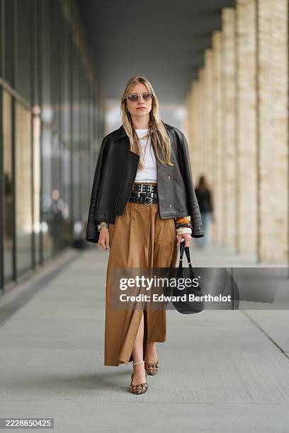 Guest wears sunglasses with a light frame and tinted lenses. Hair is styled straight and loose. A black leather jacket is layered over a white top....