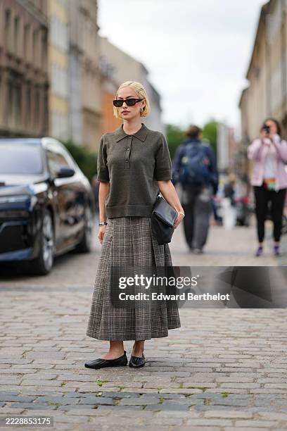 Guest wears a dark olive green short-sleeved knit polo shirt with a ribbed collar and button placket. The hair is styled in a sleek bob with...