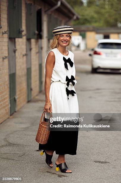 Guest wears black skirt, white top with black bows, brown bag and black and beige hat outside the Baum und Pferdgarten show during Copenhagen Fashion...