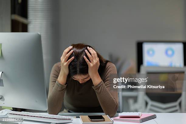 stressed businesswoman holding head in hands at office desk - esigere foto e immagini stock