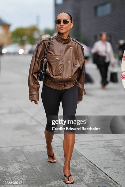 Guest wears a brown leather jacket with a high collar and button details, featuring an asymmetrical front closure and belted waist. The jacket has...