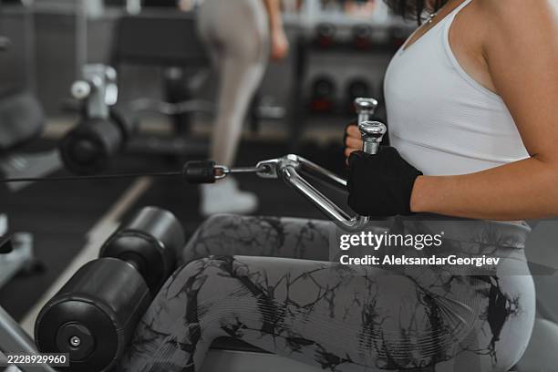 femme en bonne santé axée sur l’entraînement du dos à l’aide d’une machine à rangées assises - gants de sport photos et images de collection