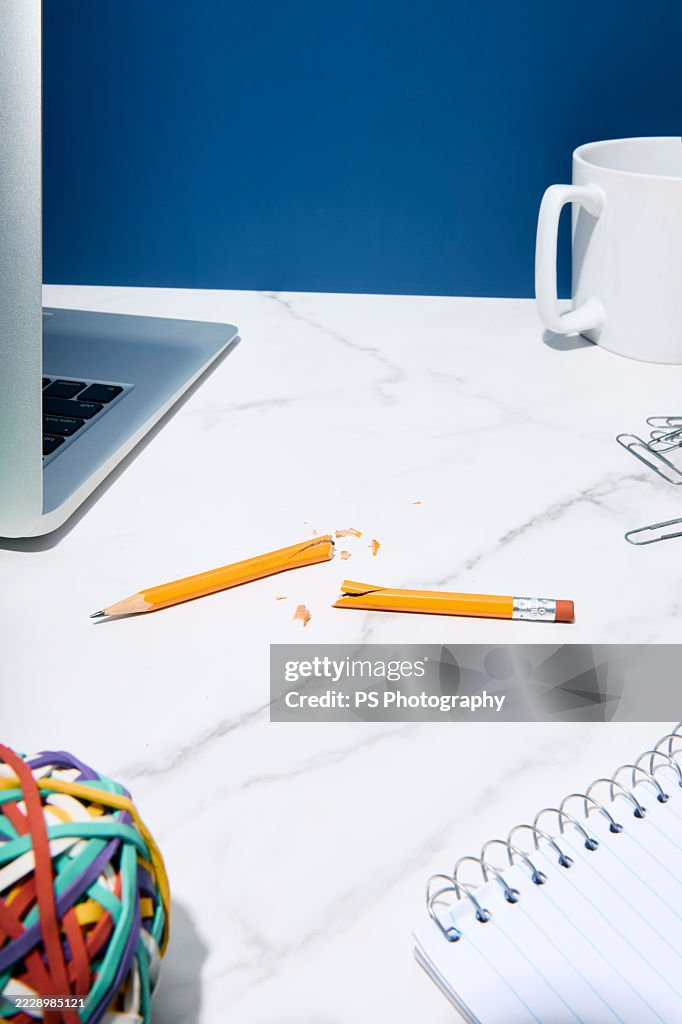 A broken yellow pencil among various office items on a desk