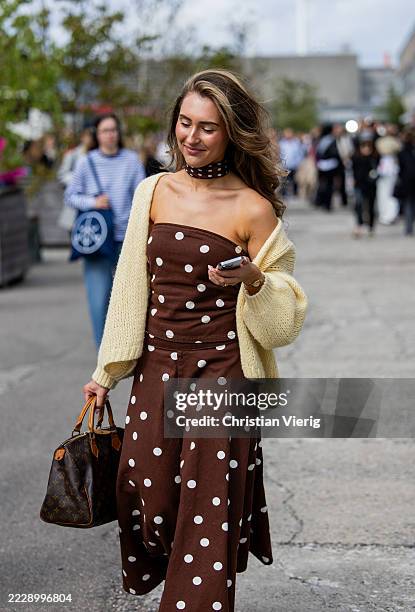 Guest wears brown white dots print dress, beige cardigan outside Marimekko during Copenhagen Fashion Week day four on August 07, 2025 in Copenhagen,...