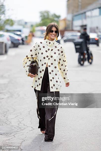 Guest wears dots print beige blouse, brown bag, pants outside Marimekko during Copenhagen Fashion Week day four on August 07, 2025 in Copenhagen,...