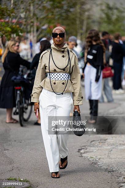 Guest wears trench jacket, white pants, black Bottega Veneta bag, head scarf outside Marimekko during Copenhagen Fashion Week day four on August 07,...
