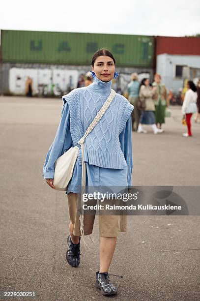 Guest wears beige shorts, blue shirt, blue knitted vest and white shoulder bag with tassels outside Cecilie Bahnsen during Copenhagen Fashion Week...