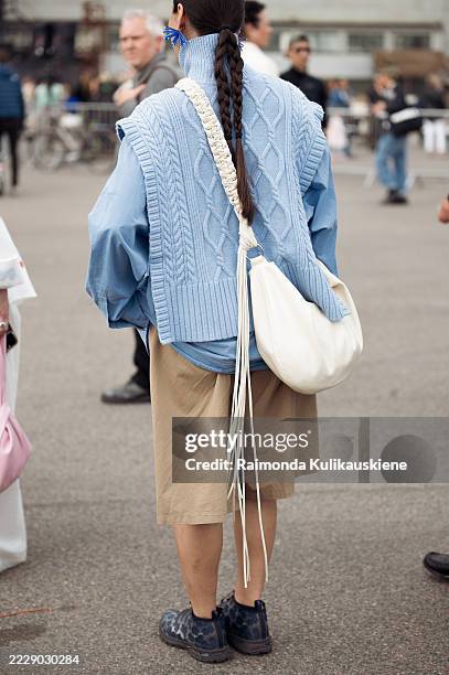 Guest wears beige shorts, blue shirt, blue knitted vest and white shoulder bag with tassels outside Cecilie Bahnsen during Copenhagen Fashion Week...