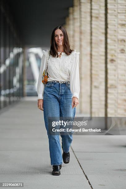 Astrid Boutrot wears a white blouse featuring intricate lace detailing along the collar and shoulders, with long sleeves ending in lace-trimmed...