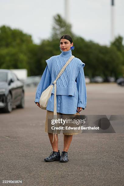 Guest wears dark brown hair parted in the center and pulled back into a low sleek bun, an oversized cobalt blue floral earring on one ear, an...
