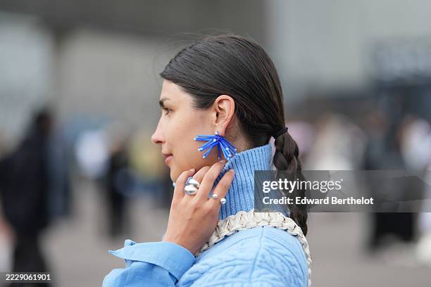 Guest wears long dark brown hair with a side part styled in a low braided ponytail secured with a black elastic, cobalt blue statement earrings built...