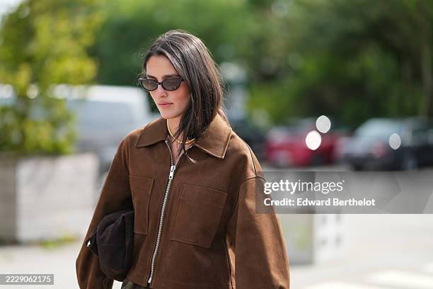Guest wears shoulder-length straight dark brown hair parted slightly off-center, narrow black rectangular sunglasses with dark lenses, a short yellow...