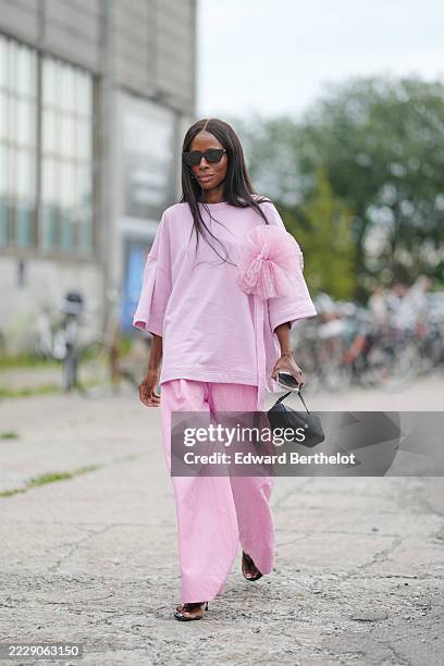 Guest wears a light pink oversized top with elbow-length sleeves, featuring a large tulle embellishment on the left shoulder. Paired with matching...