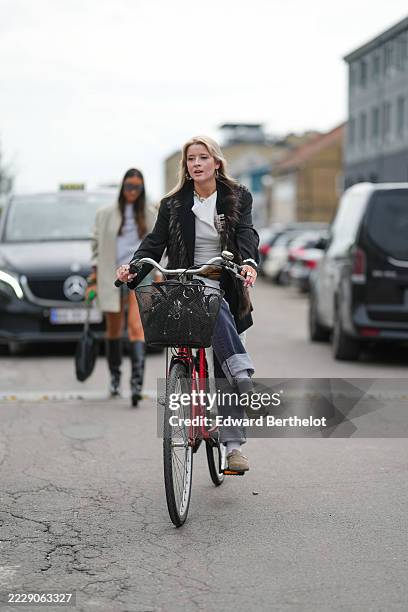 Guest wears a black pinstripe blazer with a fur collar over a white top. The outfit includes dark blue jeans with wide cuffs. Footwear consists of...