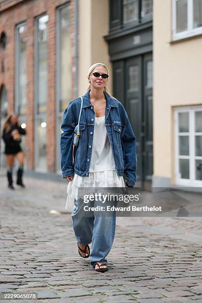 Guest wears light blonde straight hair pulled back into a low ponytail and held with a wide cream ribbed-knit headband, narrow black oval sunglasses,...