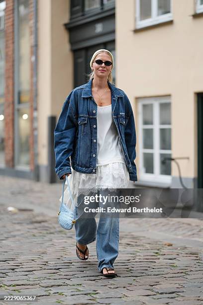 Guest wears light blonde hair slicked back into a low bun with a wide cream ribbed headband, narrow oval black sunglasses, small gold hoop earrings,...