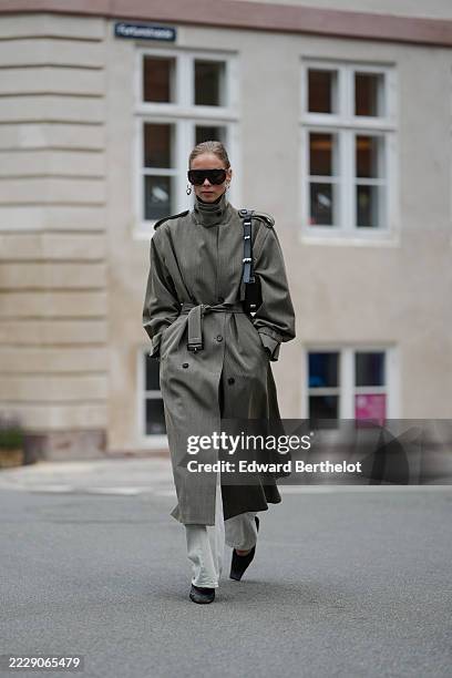 Guest wears dark blonde hair slicked back into a low bun, oversized black shield sunglasses, and a single silver hoop earring; a black crossbody bag...