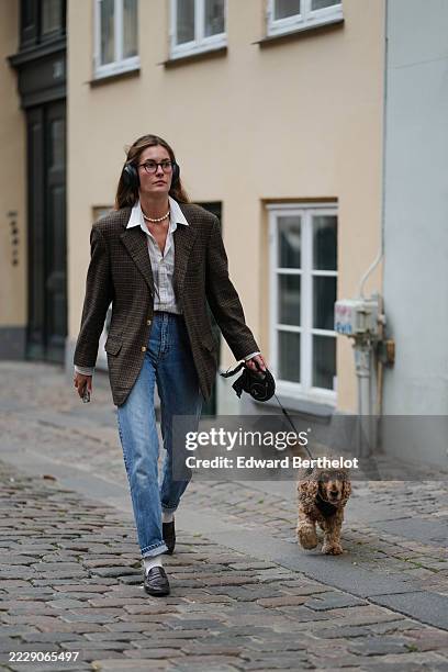 Guest wears black over-ear headphones and round black eyeglasses, with long light brown hair parted at the center and worn loose; a short pearl-bead...