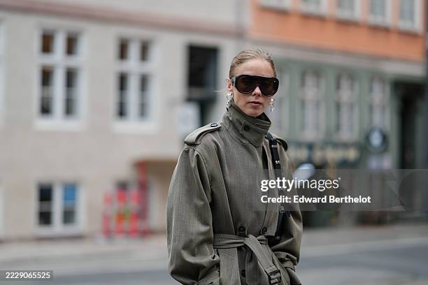 Guest wears light blonde hair styled in a neat low bun, oversized black shield sunglasses with dark lenses, silver-tone sculptural drop earrings, and...