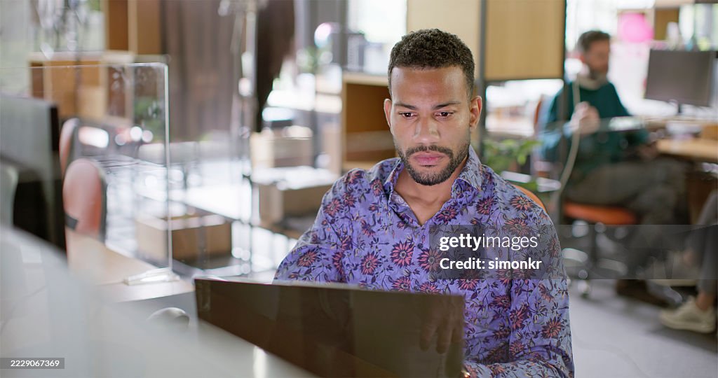 Focused Multiracial Businessman in Patterned Shirt Working on Laptop in Modern Office