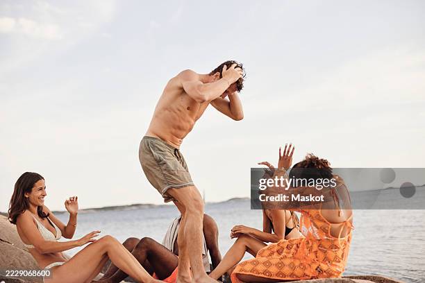 playful shirtless man having fun with friends sitting on rock formation by sea - sprinkling stock pictures, royalty-free photos & images
