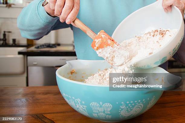 close-up of a senior woman standing in a kitchen adding flour to a bowl to make cookies - cake batter stock pictures, royalty-free photos & images