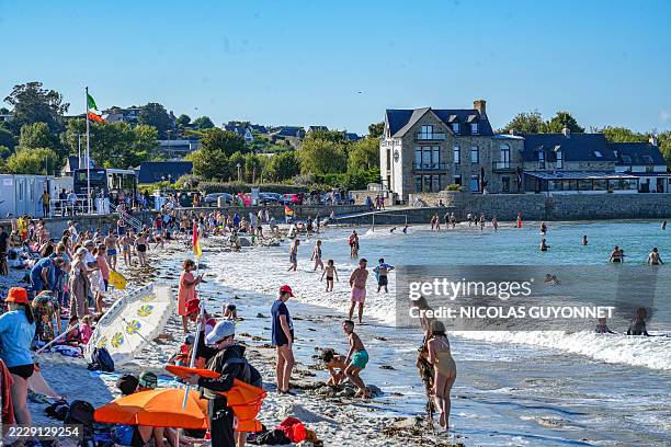 Tourists and vacationers sit and lie on their towels on the beach, others play and swim in the English Channel in Saint Pol de Leon, France, August...