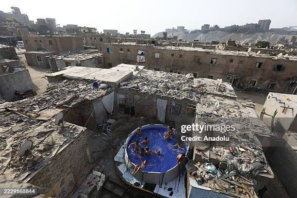 An aerial view of children swimming and playing in an above-ground pool set up on the rooftop of a building during summer in the Eldweka district of...