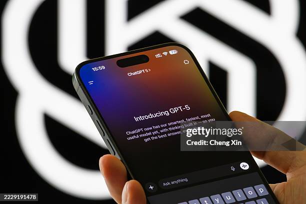 In this photo illustration, a person holds a smartphone showing the Introducing GPT-5 interface in the ChatGPT app, with text describing the model's...