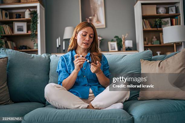 woman checking blood sugar level with glucose meter at home - glucometer stock pictures, royalty-free photos & images