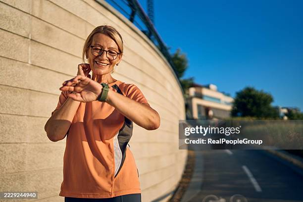 smiling senior woman checking her smartwatch during outdoor workout - fitness tracker stock pictures, royalty-free photos & images