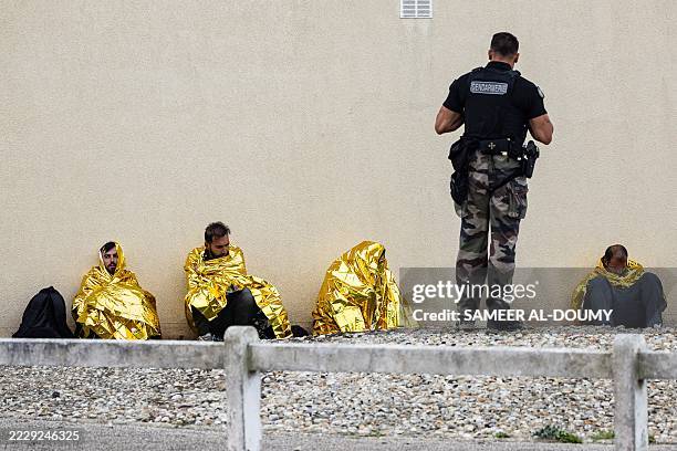 French Gendarme stands among migrants abandoned from a smuggler's boat as they sit covered with foil blankets after they attempted to cross the...