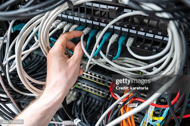 plugging ethernet cable into cluttered network rack - network cabling stock pictures, royalty-free photos & images