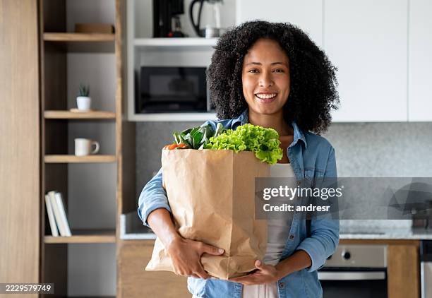happy woman arriving home carrying a bag of groceries - paper bag stock pictures, royalty-free photos & images