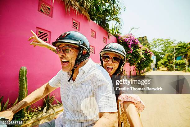 medium shot mischievous senior couple driving motor scooter on street - divertimento imagens e fotografias de stock