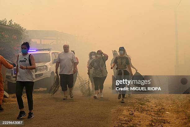 People carry branches and buckets to fight wildfire in the village of Veiga das Meas, in Villardevos municipality, northwestern Spain, on August 16,...