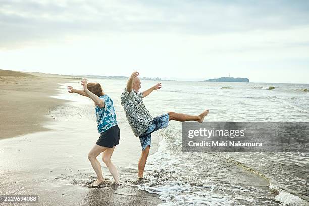 a senior couple, a man and a woman, frolic in the waves on the beach. - old woman dancing stock pictures, royalty-free photos & images