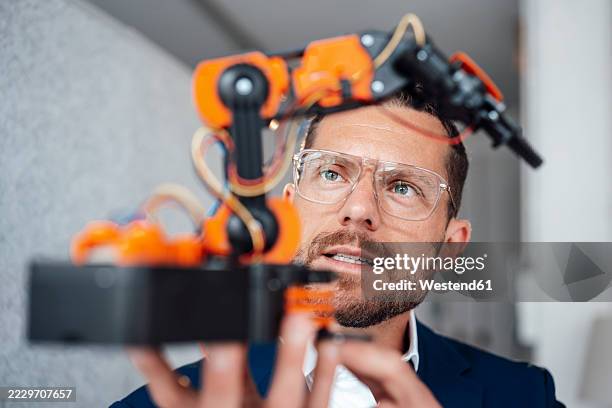 engineer wearing eyeglasses operating robotic model in office - robotic machine stock pictures, royalty-free photos & images