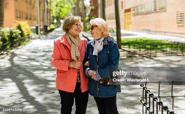 senior women enjoying a stroll through the city on a sunny day - two elderly friends chatting in a community park stock pictures, royalty-free photos & images